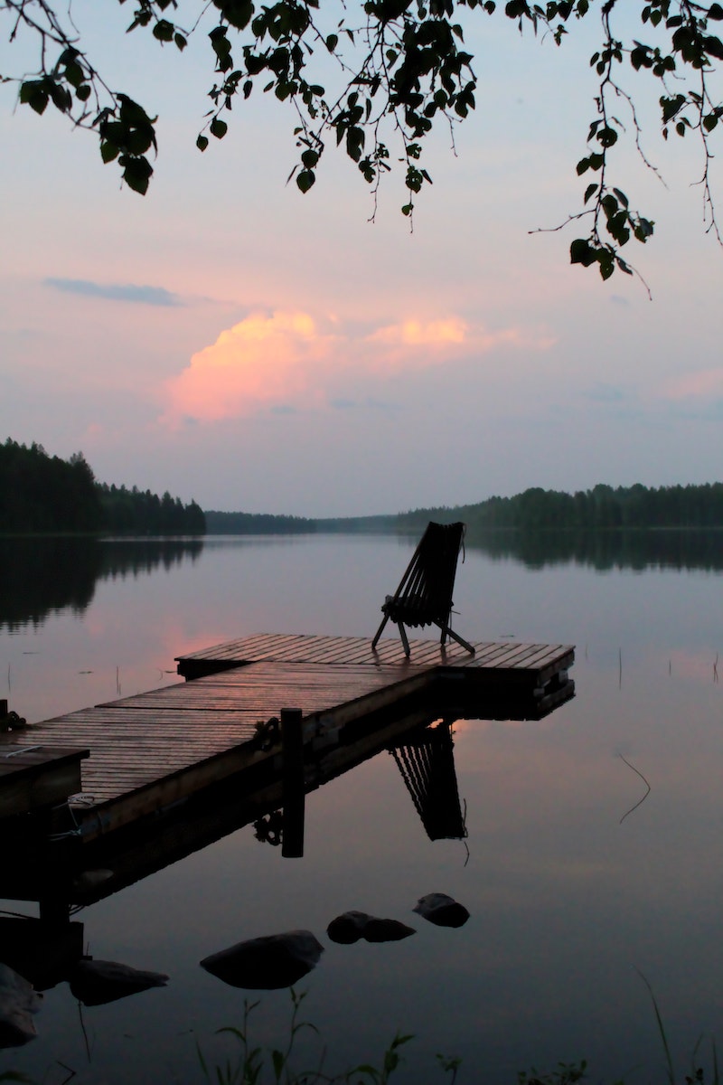 Dock with chair at end overlooking peaceful lake at sunset.